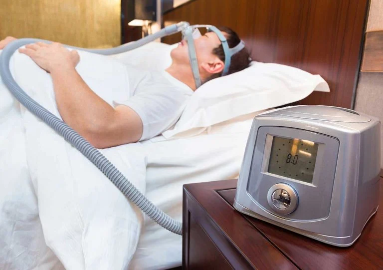 Man in bed wearing a CPAP mask with the machine on his nightstand