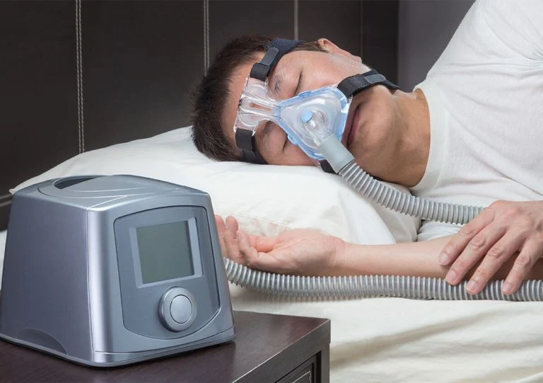 Man sleeping with a CPAP mask connected to a bedside machine