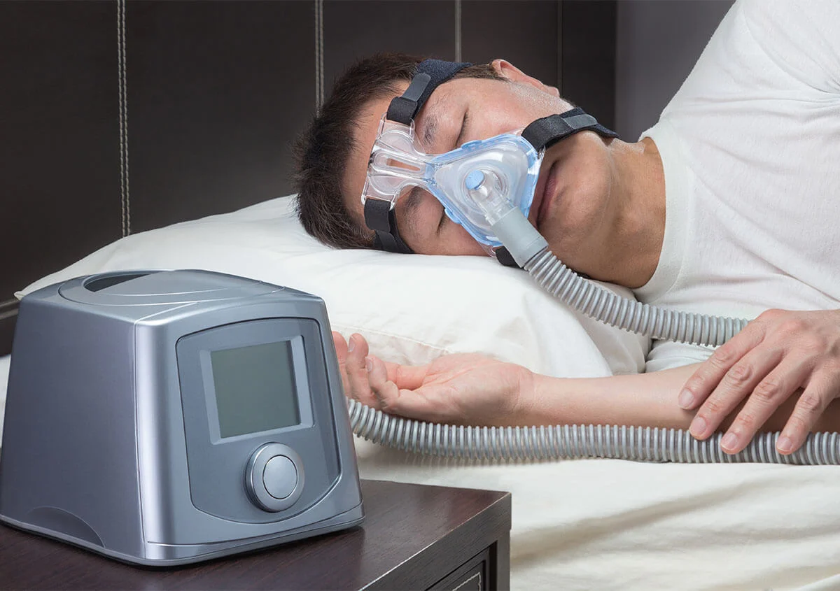 Man sleeping with a CPAP mask connected to a bedside machine
