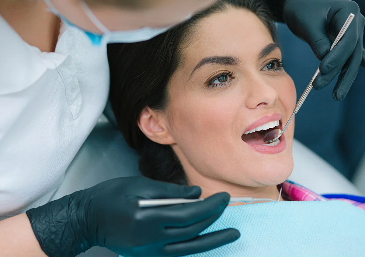 Dentist examining a smiling woman’s teeth with a mouth mirror